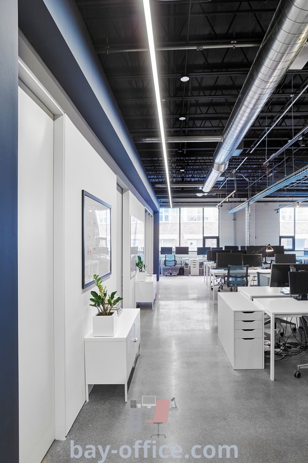 Empty office space featuring modern desks and computers along the walls, adorned with planters. This inspiring design trend highlights the best of open space office concepts and functional decor for enhancing productivity at bay-office.com.
